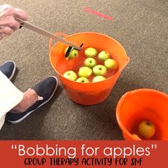 there is a person sitting on the floor with two orange buckets filled with apples