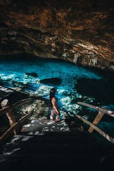 a person standing on the edge of a cave looking down at blue water and rocks