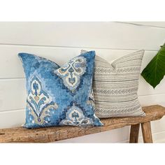 two blue and white pillows sitting on top of a wooden bench next to a plant