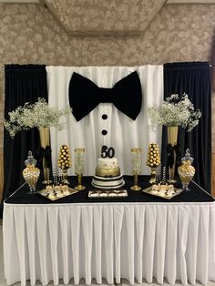 a table topped with a cake covered in white frosting and black ribboned bow ties