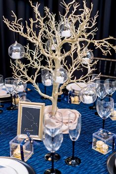 the table is set with wine glasses, plates and a tree in glass vases