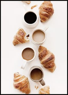 coffee and croissants are arranged on a white surface with two cups of coffee