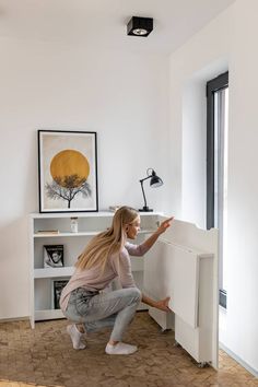 a woman kneeling down next to a white cabinet