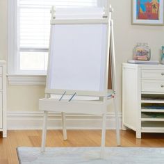 a white easel sitting on top of a hard wood floor next to a window