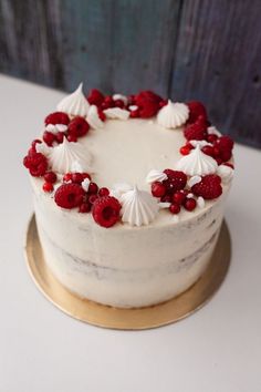 a white cake topped with raspberries and seashells on a gold plate