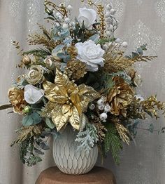 a white vase filled with lots of flowers on top of a wooden table next to a wall