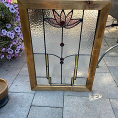 a stained glass window sitting on top of a stone floor next to purple and white flowers