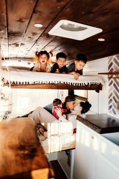 four people are hanging out in the back of a camper with bunk beds on each side