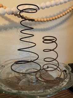 a glass bowl filled with different types of rings on top of a table next to a beaded necklace