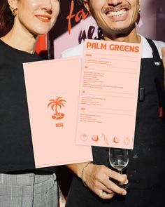 a man and woman standing next to each other holding up papers with palm greens on them