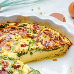 a quiche with bacon and spinach in a white pie dish next to eggs