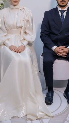 a man and woman sitting next to each other in front of a white wall with flowers