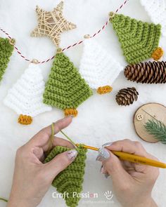 someone crocheting christmas decorations on a white surface with pine cones and needles,