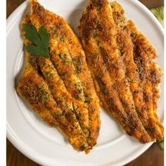 two pieces of fried fish on a white plate with parsley sprig garnish