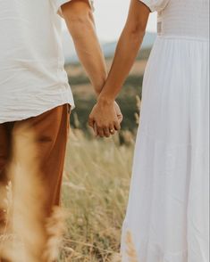 two people holding hands while standing in a field with tall grass and dry grass behind them