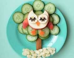 an owl made out of cucumber slices and sliced apples on a blue plate