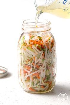 someone pouring dressing into a mason jar filled with shredded vegetables