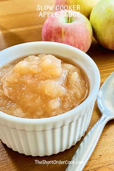 an apple sauce in a white bowl next to two apples on a wooden table with the words slow cooker apple sauce