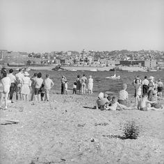 a group of people standing on top of a sandy beach next to the ocean with boats in the water