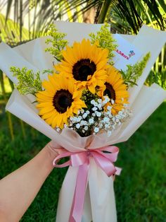 a bouquet of sunflowers is wrapped in white paper and tied with pink ribbon