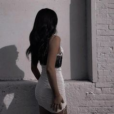 a woman standing in front of a white brick wall with her shadow on the wall