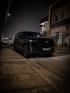 a black suv parked on the side of a street at night time with its lights on