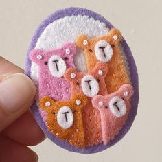 a hand holding a small brooch with three little bears on it's side