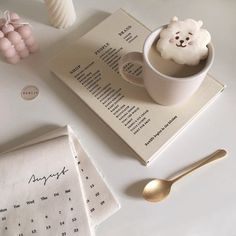 a cup of coffee on top of a table next to an open book and spoon