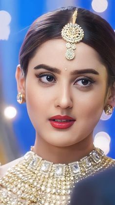 a woman with dark hair wearing a gold necklace and matching earrings, looking at the camera