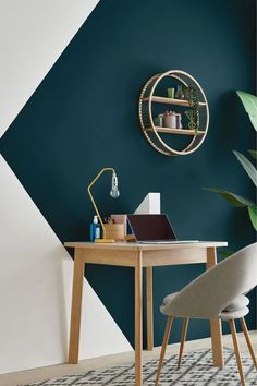 a desk with a laptop on it next to a potted plant in front of a green wall