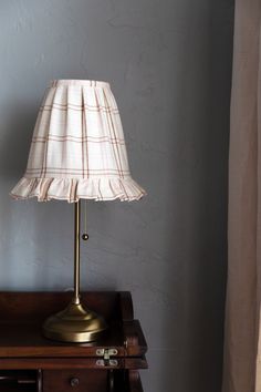 a lamp is sitting on top of a wooden table next to a window with curtains