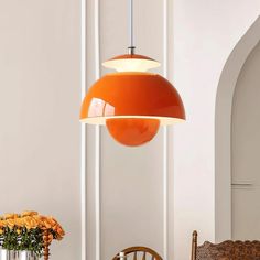 an orange lamp hanging over a dining room table with chairs and flowers in vases