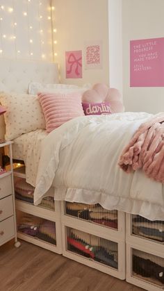 a white bed with pink pillows and blankets on top of it next to some drawers