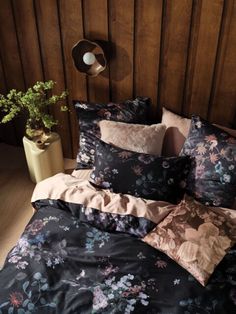 a bed covered in black and pink floral comforter next to a potted plant