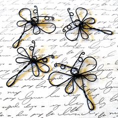 four black wire flowers sitting on top of a piece of paper with writing in the background