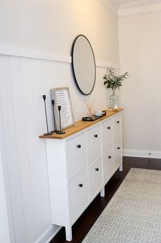 a white dresser sitting in the corner of a room with a mirror on top of it