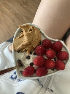 a person holding a heart shaped bowl filled with ice cream and raspberries