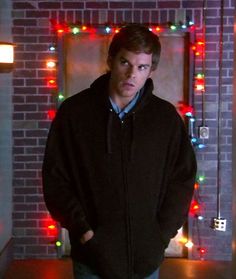 a man standing in front of a brick wall with christmas lights on the walls behind him