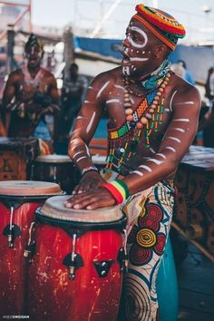 a man with painted face and body is playing the drums in front of other drummers