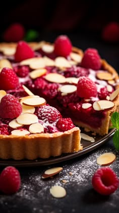 a raspberry tart with almonds on a black plate next to some raspberries