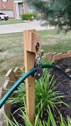 a green hose connected to a wooden post in the grass next to a flower bed