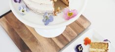 a white cake with flowers on it sitting on a wooden cutting board next to another piece of cake