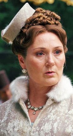 a woman wearing a white hat and fur collared coat with an elaborate braid in her hair