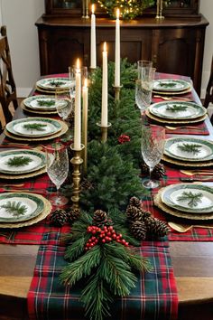 a christmas table setting with pine cones, candles and plaid napkins on the table