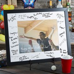 a birthday photo frame sitting on top of a wooden table next to balloons and confetti