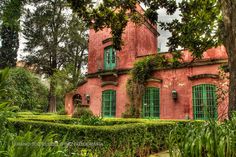 an old pink house with green shutters on the windows and bushes in front of it