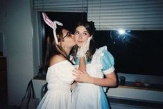 two women dressed up as alice and the rabbit kissing each other in front of a window