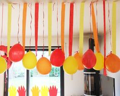 balloons and streamers are hanging from the ceiling in front of a window with flowers on it