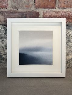 a white frame sitting on top of a floor next to a brick wall with a painting in it