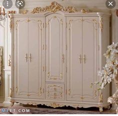 an ornate white and gold armoire in a room with flowers on the floor next to it